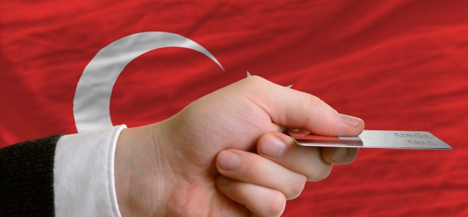 Turkey interest rate forecast for next 5 years man stretching out credit card to buy goods in front of complete wavy national flag of turkey
