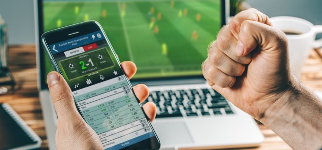A football support watches a game online while checking a mobile betting app