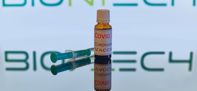 Munich/Bavaria/Germany - 11/16/2020: Coronavirus vaccine and a syringe on a white glossy surface.