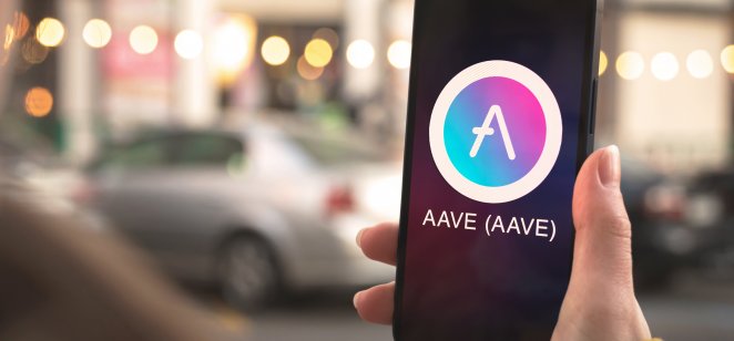 A person holding a smartphone with Aave logo on screen