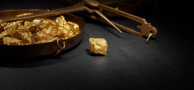 How to invest in gold: Your guide to the precious metal. Closeup of big gold nugget and scales copper