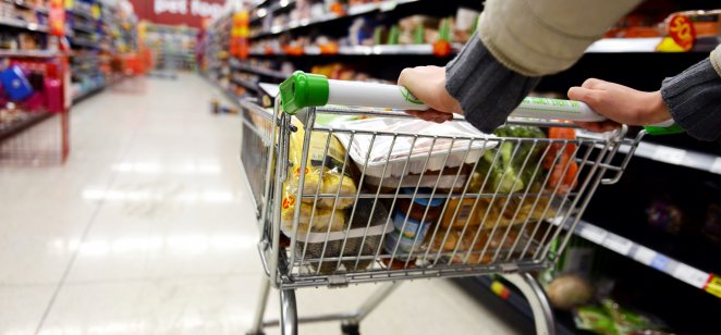 A shopper wheels a full trolley through a supermarket aisle