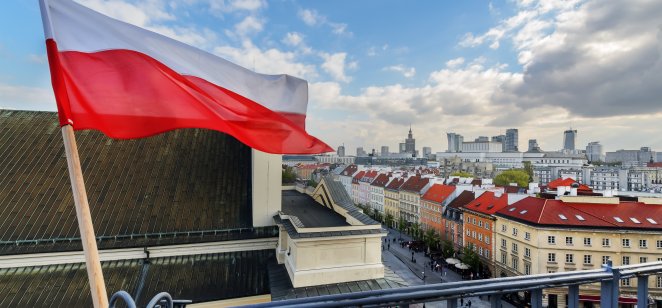 The flag of Poland in the Blue sky and the center of Warsaw in the background
