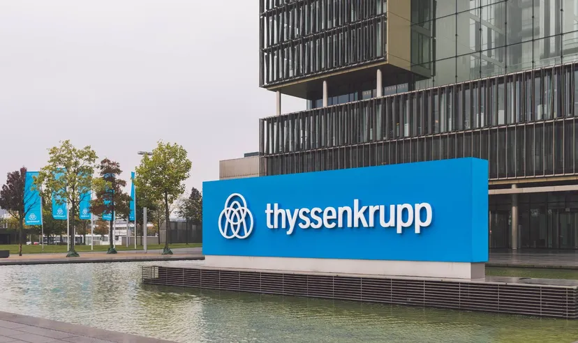 Thyssenkrupp-Logo auf einem blauen Firmenschild vor einem modernen Bürogebäude