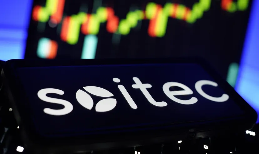 Soitec logo displayed in front of a blurred stock market chart with green and red candlesticks.