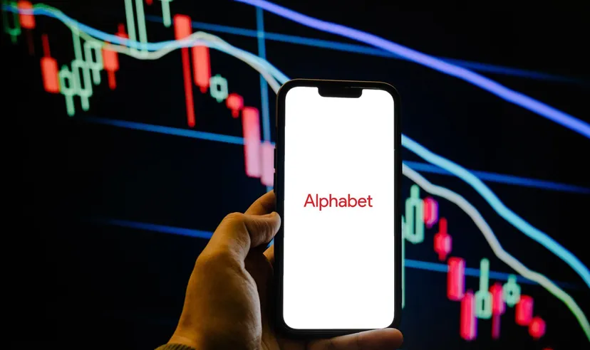 Smartphone displaying the Alphabet logo in front of a bearish candlestick stock chart, representing the technology company and its stock market performance. 