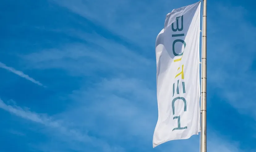 BioNTech-Flagge auf hohem Mast weht vor blauem Himmel mit leichten Wolken