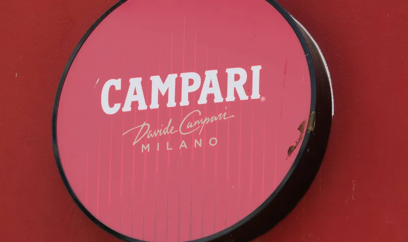 Round illuminated Campari sign mounted on a red wall with white Campari Milano branding