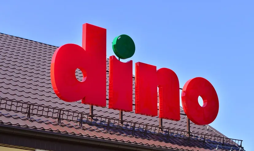 Logo supermarketu Dino umieszczone na dachu na tle czystego błękitnego nieba