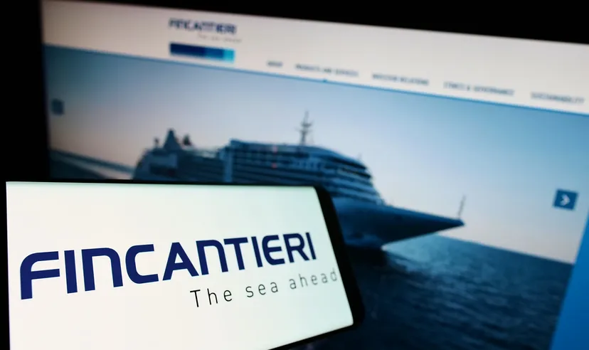 Smartphone displaying Fincantieri logo with a blurred image of a cruise ship on a website in the background