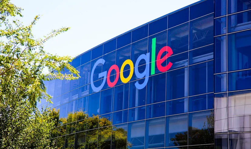 An exterior shot of the Googleplex building in Mountain View, California. it has a blue glass front with the multicoloured Google logo on it