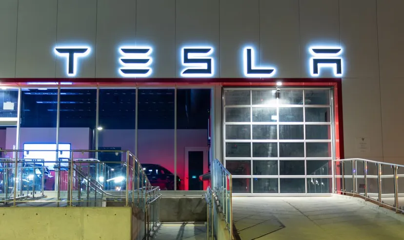 Tesla logo atop of a Tesla Dealership illuminated at night.