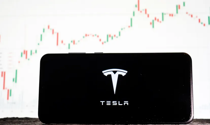 Image of Tesla logo on a smartphone against a background of stock market trends