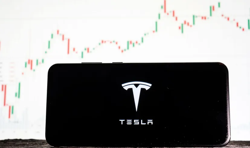 Bild des Tesla-Logos auf einem Smartphone vor dem Hintergrund von Börsentrends