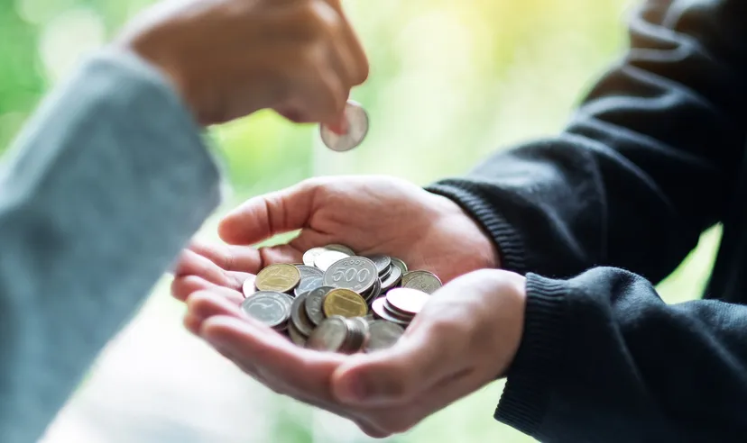 一隻手正把硬幣放入另一人捧著、裝滿零錢的雙手中。