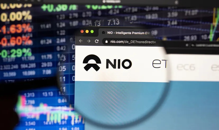 NIO stock forecast: Is it time to buy the dip? Nio electric car company logo on a website with blurry stock market developments in the background, seen on a computer screen through a magnifying glass.