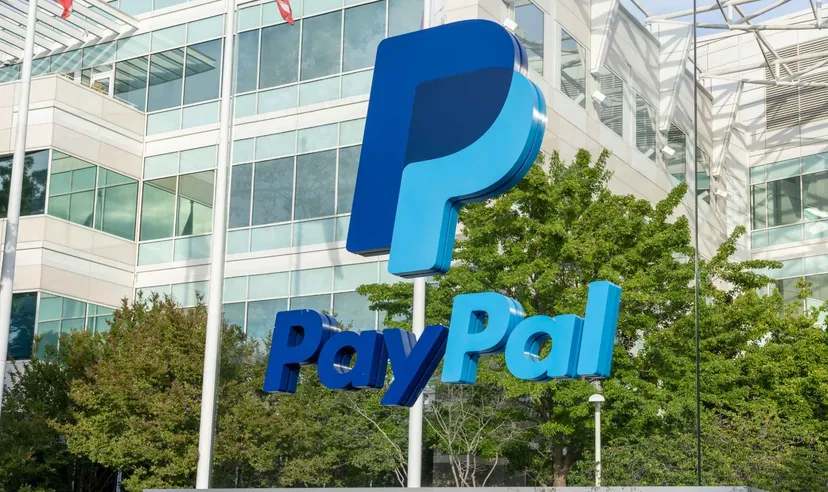 PayPal logo sign displayed outside a modern glass office building surrounded by green trees