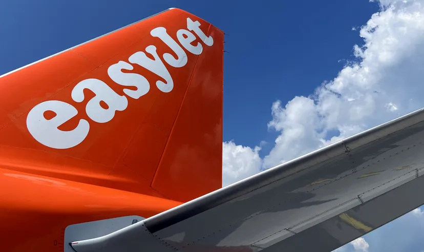 EasyJet aircraft tail and wing against a blue sky with white clouds. EasyJet aircraft tail and wing against a blue sky with white clouds.