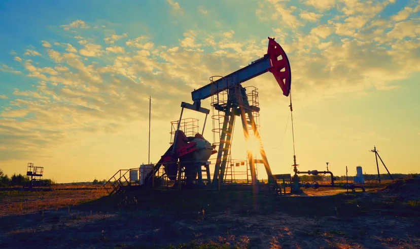 Oil pumpjack operating in an oil field at sunrise.