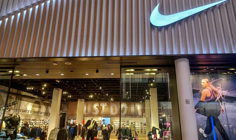 Nike-Einzelhandelsgeschäft von außen mit beleuchtetem Nike-Logo über dem Eingang und Sportbekleidung im Inneren.