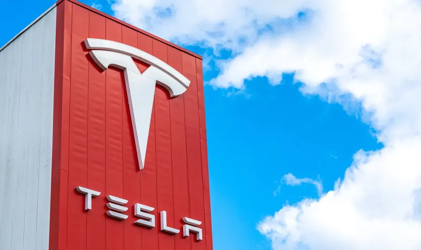 Logo Tesla na czerwonej fasadzie budynku na tle jasnego błękitnego nieba