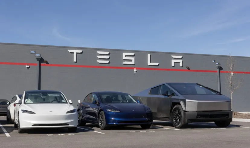 Véhicules Tesla stationnés devant un bâtiment de l'entreprise avec le logo de la société affiché sur le mur sous un ciel bleu dégagé