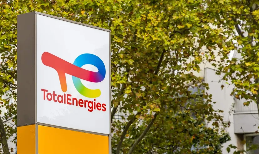 Logo TotalEnergies affiché sur un panneau extérieur avec des arbres et des bâtiments en arrière-plan