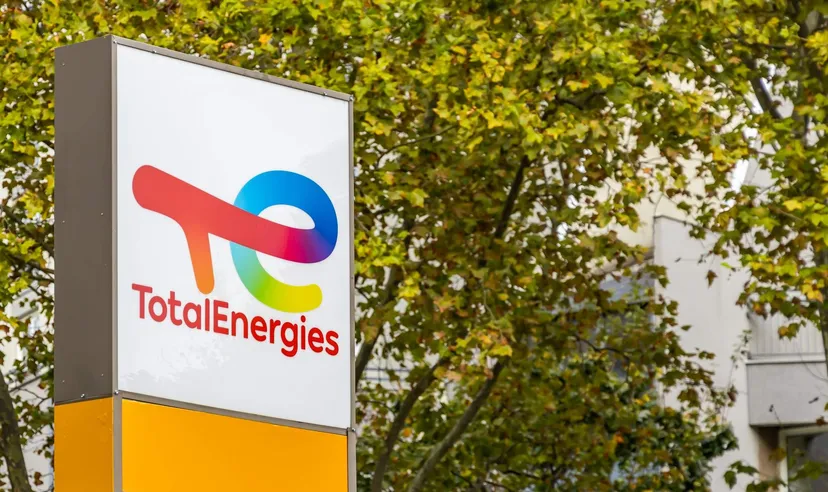 TotalEnergies logo displayed on a sign outdoors with trees and buildings in the background