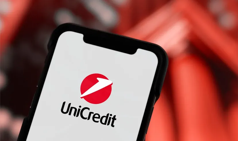 Primo piano di uno smartphone che mostra il logo UniCredit su sfondo rosso sfocato.