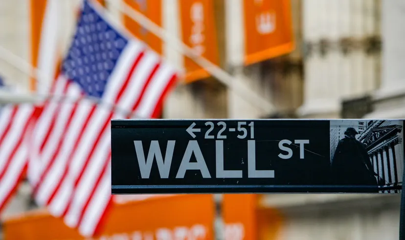 Cartello di Wall Street con bandiera americana sullo sfondo davanti al New York Stock Exchange.