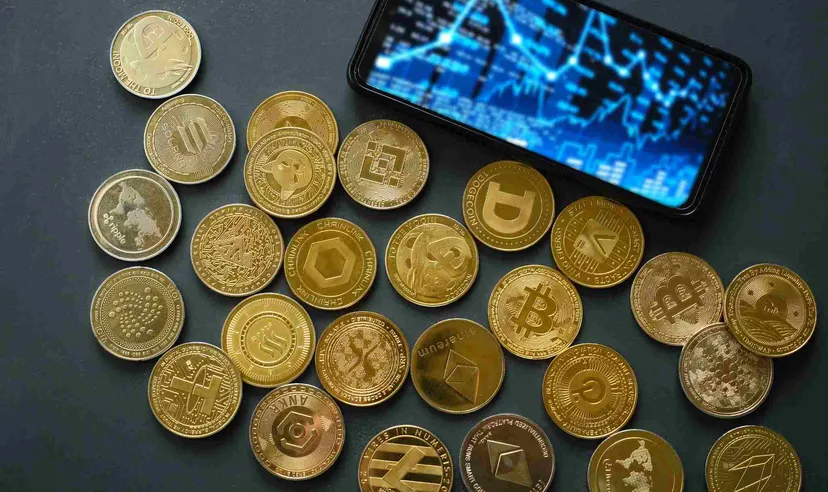 Collection of cryptocurrency coins beside a smartphone displaying a digital market chart, representing crypto trading, blockchain assets, and cryptocurrency markets.