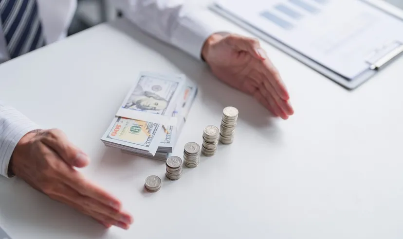Hands framing stacks of coins and US dollar banknotes on an office desk, illustrating savings, investment growth, and personal finance planning.