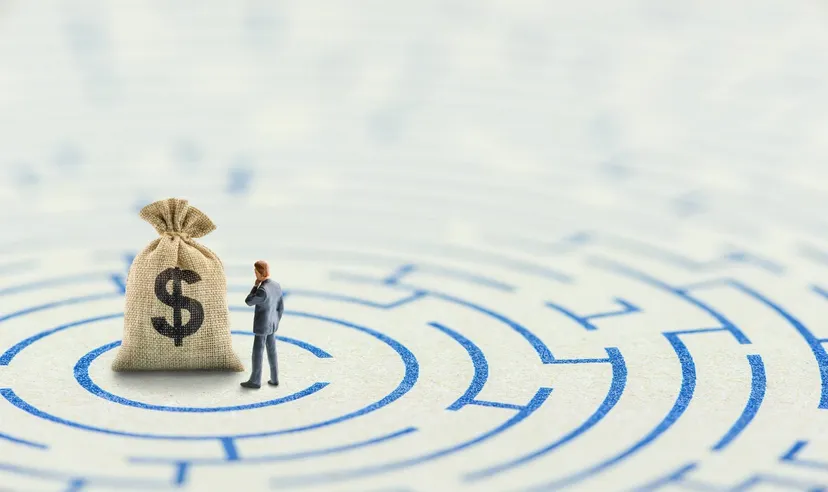 Miniature person standing beside a money bag in the centre of a maze, symbolising financial planning, investment decisions, and wealth management.
